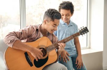 Teenage boy with his little brother playing guitar at home�