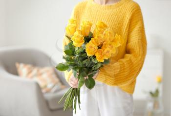 Young woman with beautiful yellow roses in room�