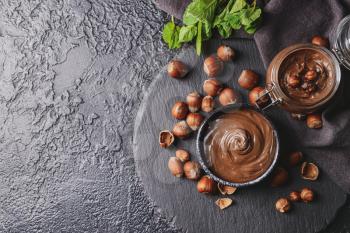 Bowl and jar with tasty chocolate paste and hazelnuts on dark background�
