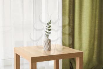 Table with vase near light curtains in room�