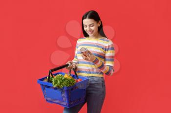 Young woman with shopping basket on color background�