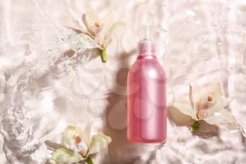 Bottle of cosmetic product and flowers in water on light background�