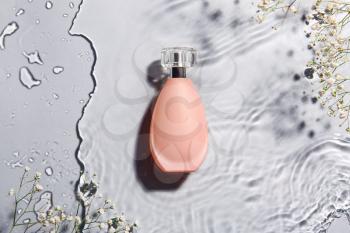 Bottle of perfume and flowers in water on grey background�