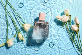 Bottle of perfume and flowers in water on color background�