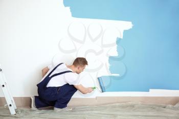 Male decorator painting wall with roller indoors�