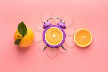 Alarm clock with ripe oranges on color background�