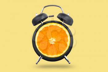 Ripe orange in alarm clock on color background�