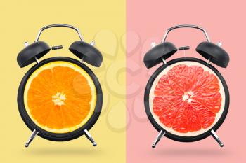 Different citrus fruits in alarm clocks on color background�