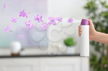 Woman spraying floral air freshener at home�