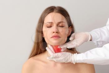 Endocrinologist examining young woman with thyroid gland problem against light background�