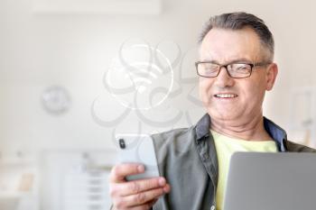 Mature man with laptop and mobile phone using wifi at home�