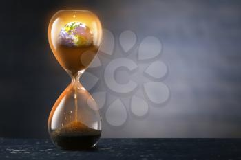 Hourglass with crumbling Earth on dark background. Concept of time�