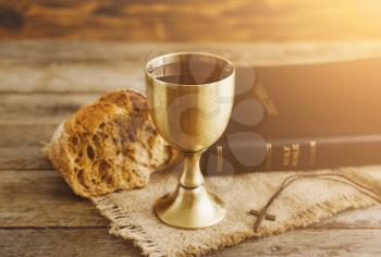 Chalice of wine with bread and Holy Bible on wooden background�