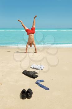 young businessman doing handstand on the beach after a big deal