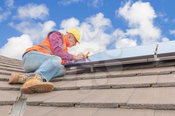 experienced worker checking solar panels on house roof