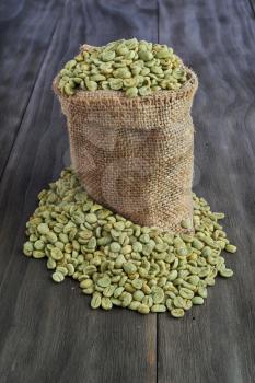 Green coffee beans in burlap sack on old wooden table