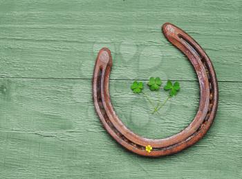 Old horseshoe and clover leaves on vintage wooden background