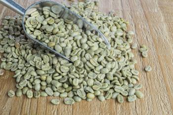 Green coffee beans in metal scoop on vintage wooden surface