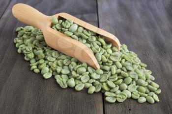 Green coffee beans in wooden scoop on vintage wooden surface