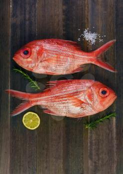 Two fresh red snappers preparing for cooking with lemon and rosemary on wooden background. Top view.
