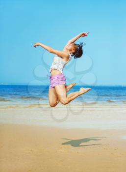 Beautiful energetic young woman jumping on the beach