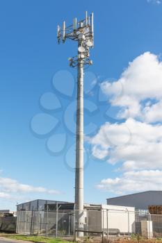 Communications Cell phone Tower against blue sky near industry buildings