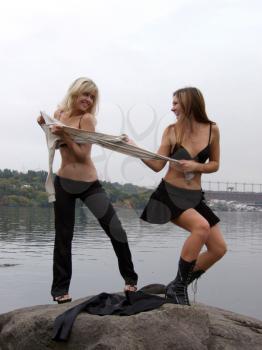Royalty Free Photo of Two Women Tugging on a Shirt Beside the Water
