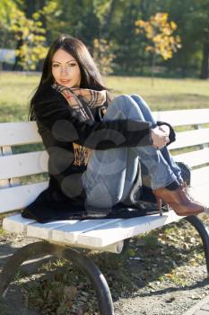 Beautiful young woman sitting on a bench in autumn park