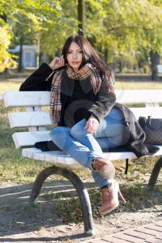 Charming young woman sitting on a bench in autumn park
