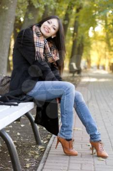 Happy young brunette sitting on a bench in autumn park
