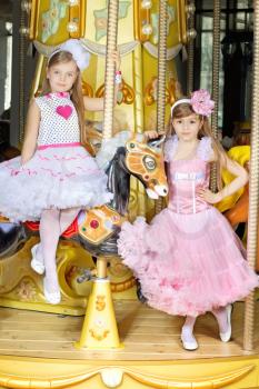 Two little girls in beautiful dresses posing on the carousel