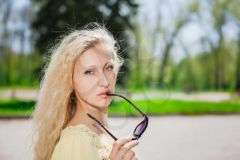 Portrait of attractive blond woman posing with sunglasses in the park