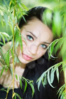 Thoughtful young brunette posing in the green branches