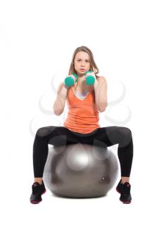 Young beautiful woman sitting on a fit doing exercises with dumbbells. Isolated