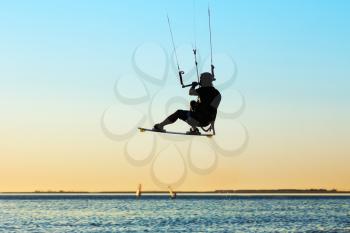 Silhouette of a kitesurfer flying above the water at sunset