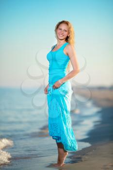 Young smiling blond woman in blue t-shirt and skirt posing near the sea