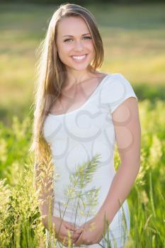 Smiling young blonde wearing white dress posing outdoors