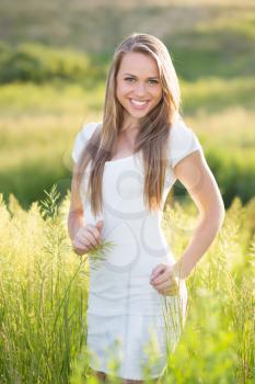 Cheerful young blonde wearing white dress posing on the meadow