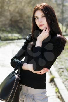 Young thoughtful lady with black bag posing outdoors