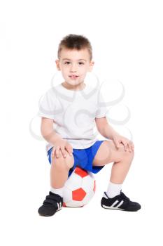 Nice little boy in football uniform sitting on his ball. Isolated on white