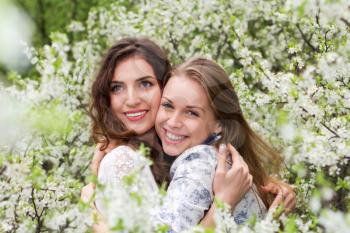 Two pretty smiling women hugging in blooming garden