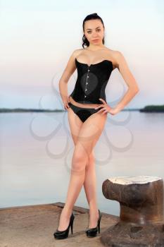 Sexy leggy woman in black panties and corset posing on the pier