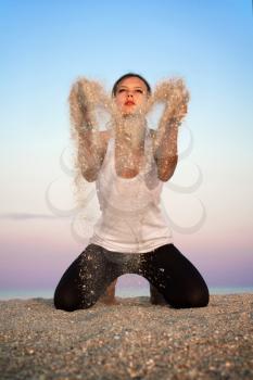 Young woman sitting on the beach and throwing sand
