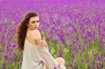 Sexy curly brunette showing her bare shoulder in a flowering field
