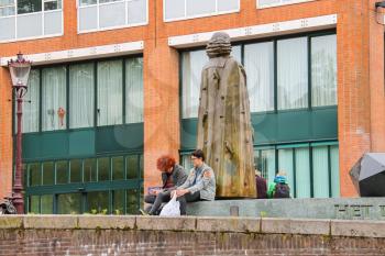 Amsterdam, Netherlands - June 20, 2015: People sit near the statue of Spinoza on the waterfront of canal in Amsterdam