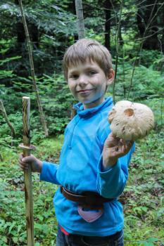 Smiling boy in forest with large mushroom in his hand