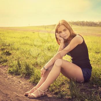 Young sensual smiling blond woman sitting on the grass outdoors