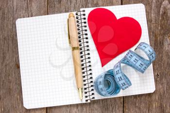 Royalty Free Photo of a Heart, Tape Measure and Pen on a Notebook