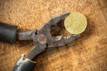 Euro cent and pliers on the wooden background. Money concept. 