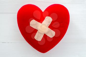 Injured heart with plaster on the white wooden surface